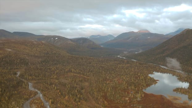 Aerial view of autumn colorful forest, lakes and swamps under the cloudy sky. Clip. Hilly terrain, wild natural landscape, Taiga, Russia