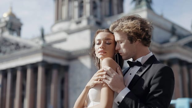 Portrait of a groom man hugging from the back happy young bride in white dress. Action. Wedding photosession in front of St. Isaac 's Cathedral, Saint Petersburg, Russia