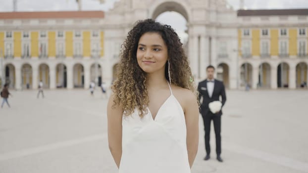 Beautiful woman in dress on background of man with bouquet of flowers. Action. Attractive woman in dress is waiting for date. Surprise man with flowers behind back of beautiful woman.