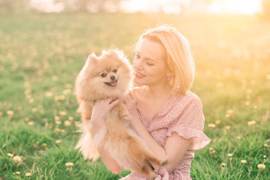 Attractive young woman holding dog spitz outside and smiling at camera, walking in park.