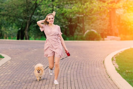 Portrait of a young glamorous female wearing pink dress holding her cute pomeranian spitz on hands. . Friendship between dogs and humans.