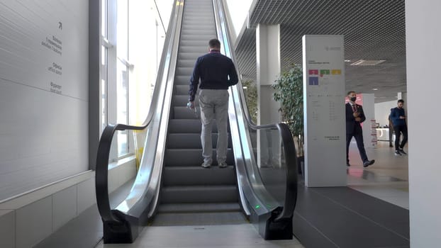Young man climbs escalator in business building. HDR. Rear view of man climbing on escalator. Man climbs an escalator in bright building with large windows.