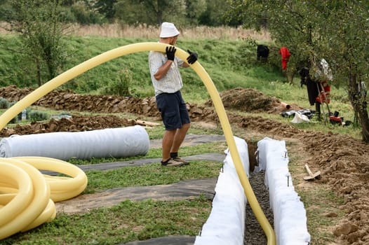 Groundwater drainage works in the field. A worker carries a yellow perforated drainage pipe.