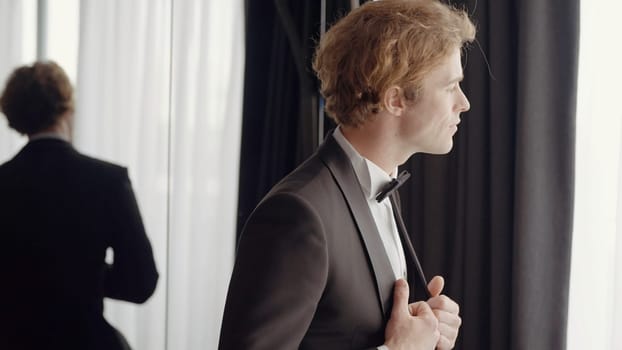 A man with a sympathetic appearance . Action . A man in an elegant suit stands next to the mirror and poses