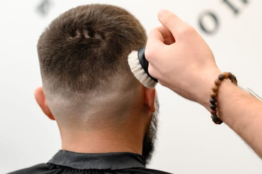 Barber sweeps hair with a brush while cutting a clients hair in a salon.