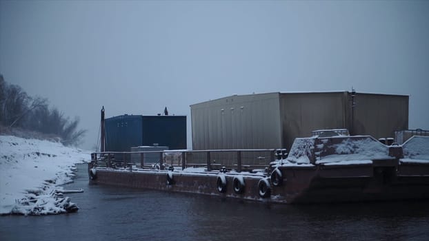 Barge with containers on river in winter. Clip. Barge transports cargo with containers along river in winter. Winter river transportation by barge.