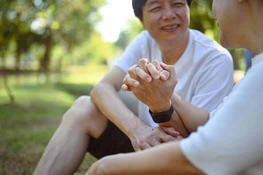 Happy senior couple holding hands and looking at each other while sitting in summer park