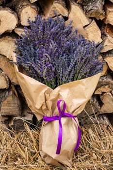 A lush and large bouquet of lavender wrapped in brown paper on a background of firewood