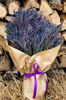 A lush and large bouquet of lavender wrapped in brown paper on a background of firewood