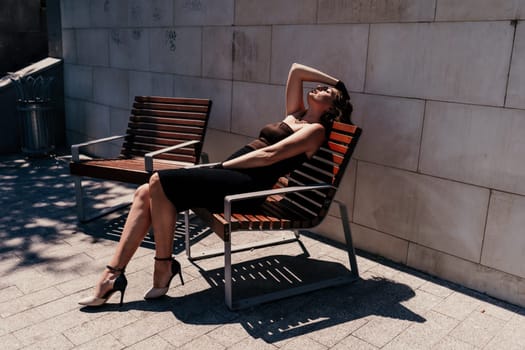 Portrait of a woman on the street. An attractive woman in a black dress is sitting on a bench outside