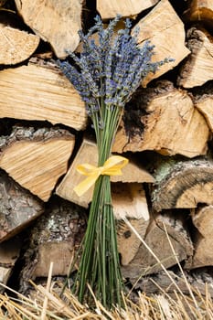 A small bouquet of lavender with a yellow ribbon on a background of firewood.