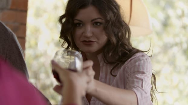 Close up of women clinking glasses with wine at a party. Stock. Summer background with green blurred leaves and people drinking wine