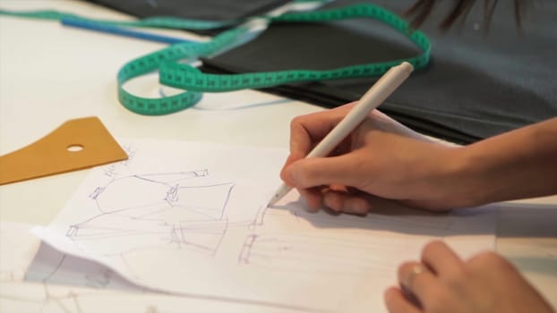 Female tailor stitching material at workplace. Preparing fabric for clothes making. Tailoring, garment industry, fashion designer sketch drawing costume concept and tailor draws sketches. Designer workshop concept. Tailor At Work In Small Business: Fashion Design. Close Up
