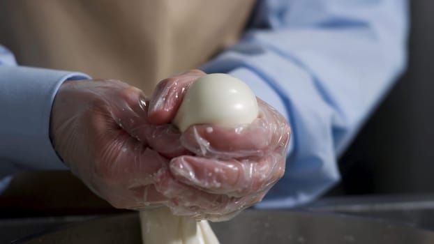 Close up for hands of a cheesemaker cutting mozzarella with hands, traditional food concept. Process of making delicious italian cheese.