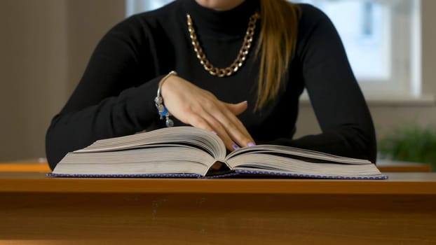 Women's hands leafing through a book. Woman sitting at the table leafing through the book.