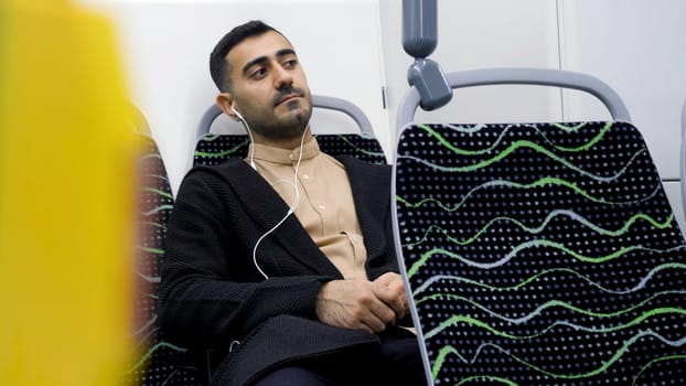 Portrait of handsome man in headphones listening to music in public transport. Media. Young man in empty bus looking thoughtfully