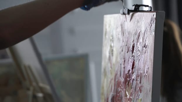 Art painting with palette knife. Side view of an artist hand in latex glove using professional palette knife for creating a masterpiece.
