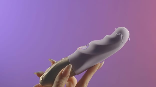 Faloimitator.Creative.A small gray vibrator on a gentle background in the hand on which grease is poured. High quality 4k footage