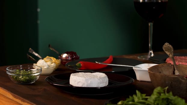 Close up of the ingredients and different sauces on the wooden table. Cheese camembert, red hot chili pepper , and greenery for burger preparation.