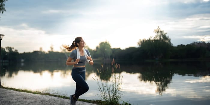 Jogging woman running in park on beautiful day off. Sport fitness model of asian ethnicity training outdoor for marathon.