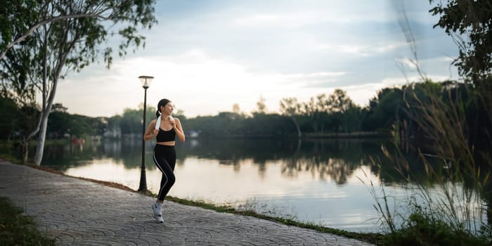 Jogging woman running in park on beautiful day off. Sport fitness model of asian ethnicity training outdoor for marathon.