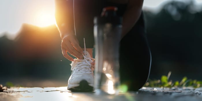 Young woman ties shoelaces while stretching stretch during stretching exercise outdoors in the park.