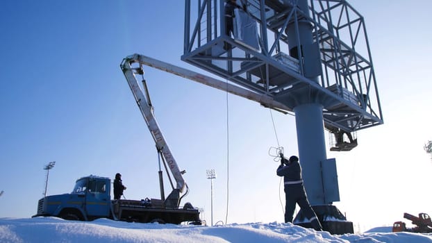 Men assemble Billboard on tap. Builder on a Lift Platform at a construction site. Man rises to the top part of the Billboard for advertising.