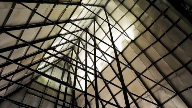 Metal sections of the roof of an industrial warehouse. Bottom view of triangular roof made of plywood sheets with steel structure of metal beams.