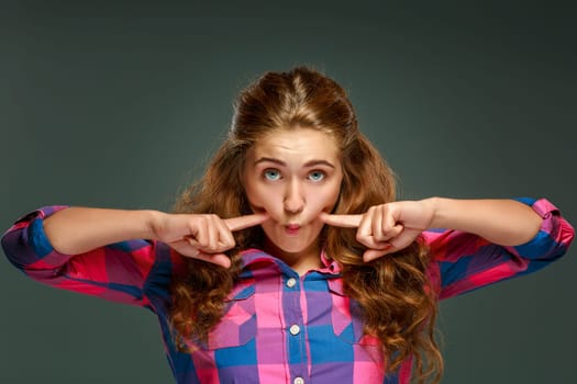 Portrait playful young brunette woman with wavy hair, looking at the camera, isolated on dark background