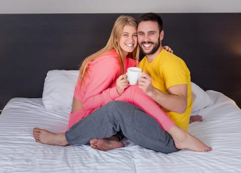 Happy young couple having breakfast tray on bed at home in bedroom. Young couple drink coffee in bed, happy smile