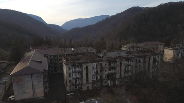 Old settlement at the top of mountain hill. Aerial view of the old abandoned residential buildings surrounded by mountains with trees.