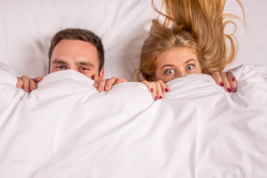 Young lovely couple lying in a bed, looking at camera, cover under blanket top angle view up above