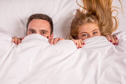 Young lovely couple lying in a bed, looking at camera, cover under blanket top angle view up above