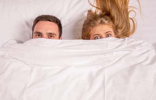 Young lovely couple lying in a bed, looking at camera, cover under blanket top angle view up above