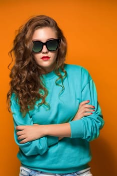 Portrait beautiful young brunette woman with wavy hair, on sun glasses, on orange background