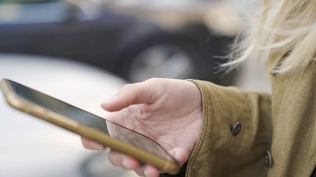 Close-up of woman typing on phone. Media. Woman uses phone on street. Modern touch-sensitive smartphone in hands of young woman.