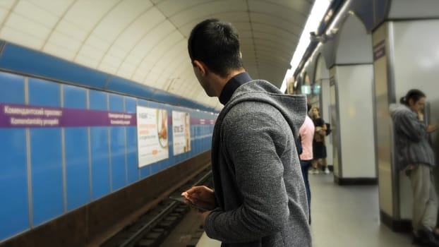 Man uses tablet in subway. Media. Young man uses tablet while waiting for train in metro. Young man is waiting for metro train with tablet in hands.