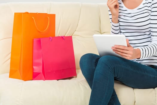 Online shopping and technology concept - smiling beautiful young woman with tablet pc computer and credit card. She sit on sofa with colorful bags