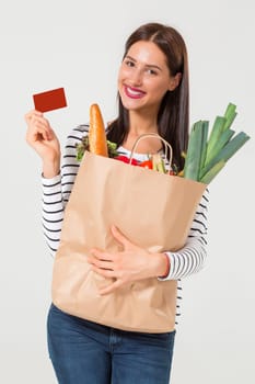 Beautiful young woman with credit card holding groceries in eco paper bag. Female consumer in shop. Concept of online shopping