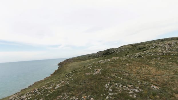 Aerial view of green hills and stones on cloudy sky and sea background. Shot. Flying above beautiful mountain top