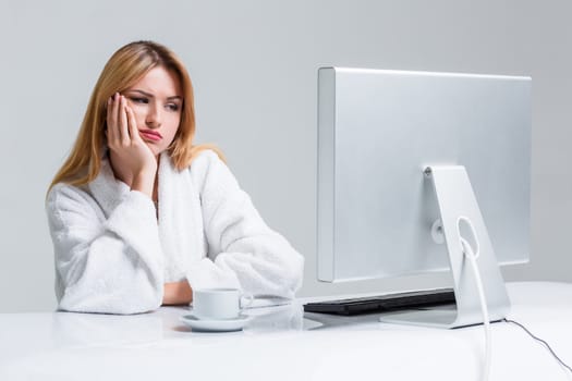 young woman sitting in the table and using computer on gray background. sleepy in the morning looking at the monitor