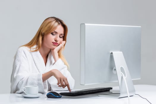 young woman sitting in the table and using computer on gray background. sleepy in the morning looking at the monitor