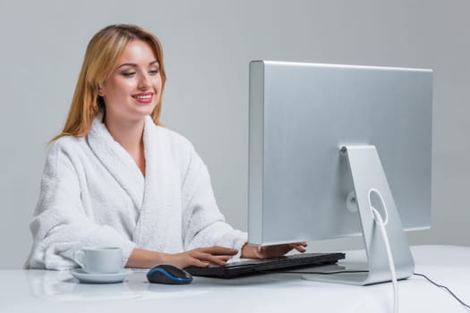 young woman sitting in the table and using computer on gray background. girl smiling and looking at monitor