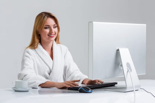 young woman sitting in the table and using computer on gray background. girl smiling and looking at monitor