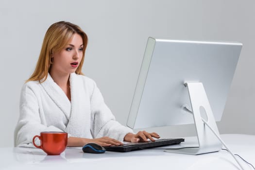 young woman sitting in the table and using computer on gray background. Surprised by the image on the monitor