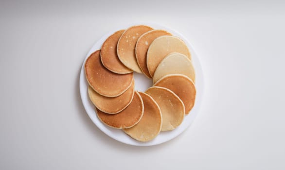 Plate with many round pancakes standing on white background top view. Delicious breakfasts concept