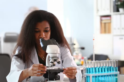 Black woman scientist student chemist in protective goggles are conducting research using microscope for bacterial contamination of water to search for vaccine to treat diseases in medicine.