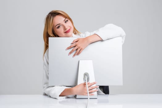 young woman sitting in the table and using computer on gray background. satisfied smiling girl hugging Monitor