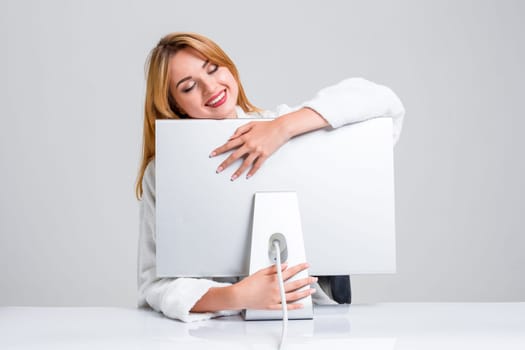 young woman sitting in the table and using computer on gray background. satisfied smiling girl hugging Monitor