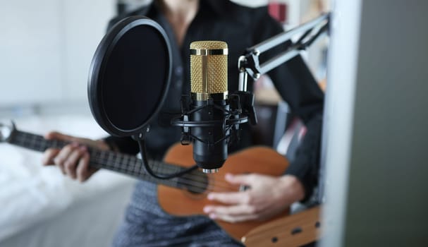 Gold modern professional microphone against woman with ukulele closeup background. Music education concept